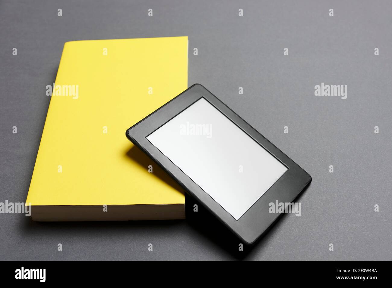 Elektronisches Lesegerät mit leerem Bildschirm und geschlossenem gelben Buch auf grauem Hintergrund. Konzepte der Technik und des Lesens. Bild mit Kopierbereich. Stockfoto