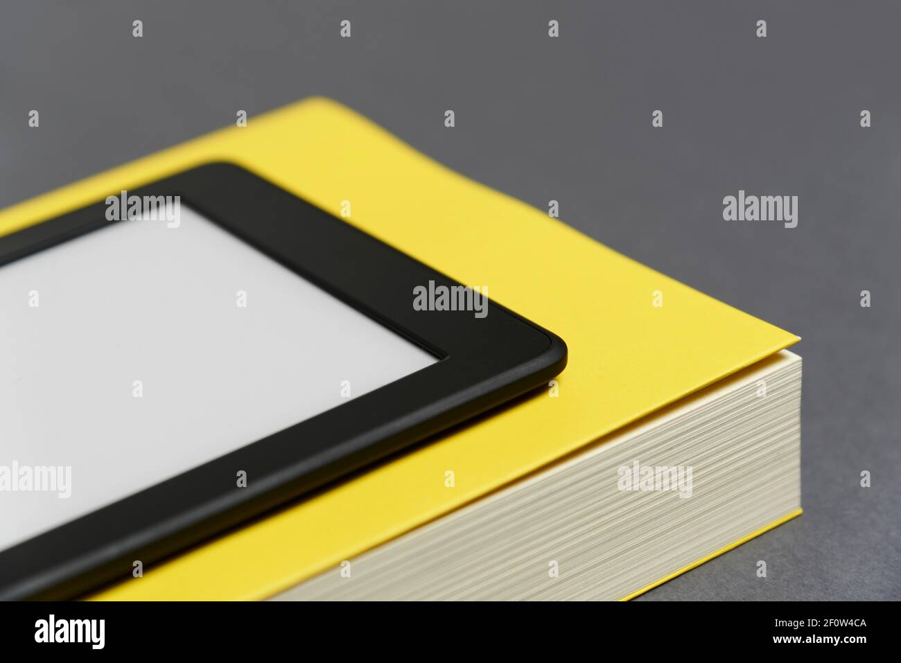 Elektronisches Lesegerät mit leerem Bildschirm und geschlossenem gelben Buch auf grauem Hintergrund. Konzepte der Technik und des Lesens. Bild mit Kopierbereich. Stockfoto