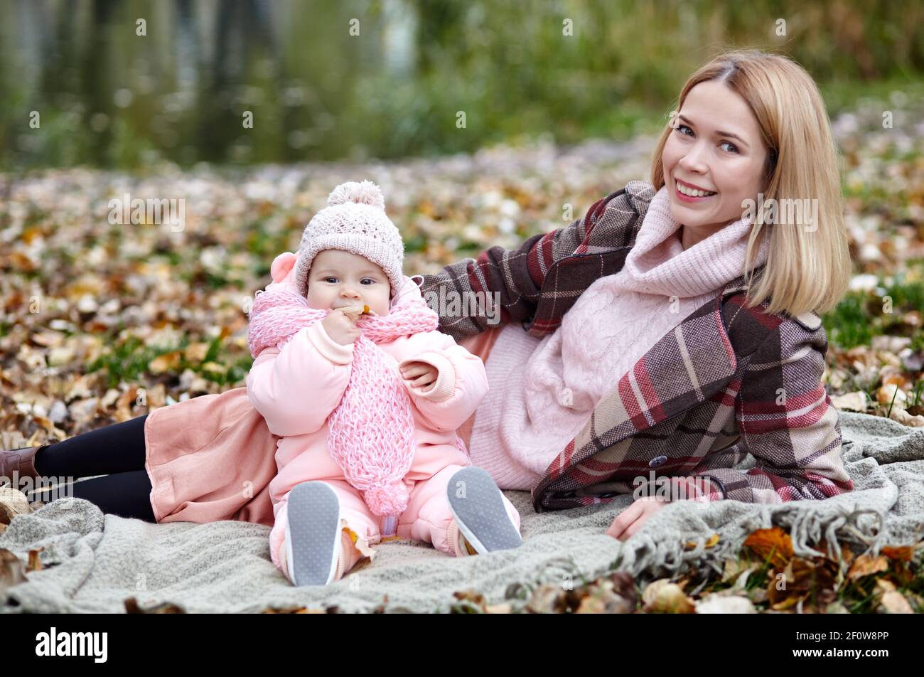 Schöne Baby-Mädchen mit Mutter auf dem Plaid sitzen. Familien im Freien. Liebenswert kleines Mädchen in warmen Kleidern bei Picknick im Herbst Park an sonnigen Tag. Pret Stockfoto