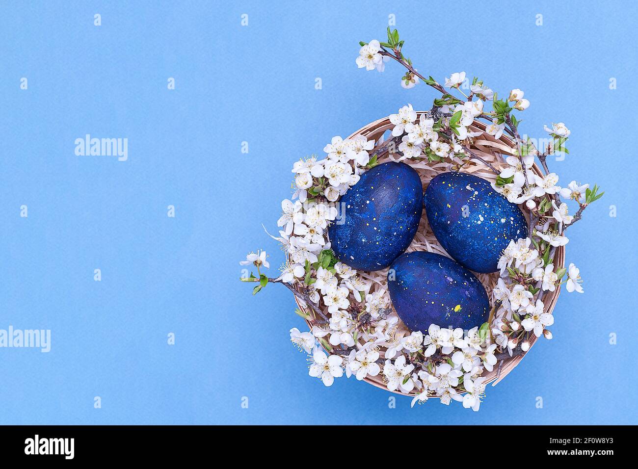 Blaue ostereier in einem Korb mit Blumen auf blauem Hintergrund. Horizontales Foto. Draufsicht Stockfoto