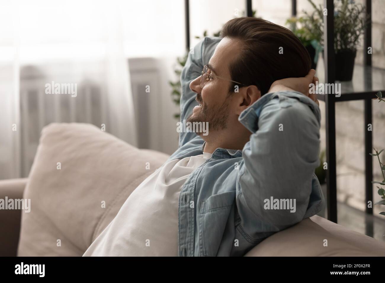 Happy Millennial Mann sitzen auf dem Sofa Hände hinter dem Kopf halten Stockfoto