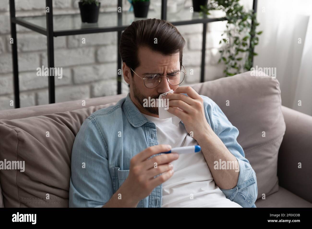 Millennial Mann fühlen sich krank wischen Nase sehen Fieber auf Thermometer Stockfoto