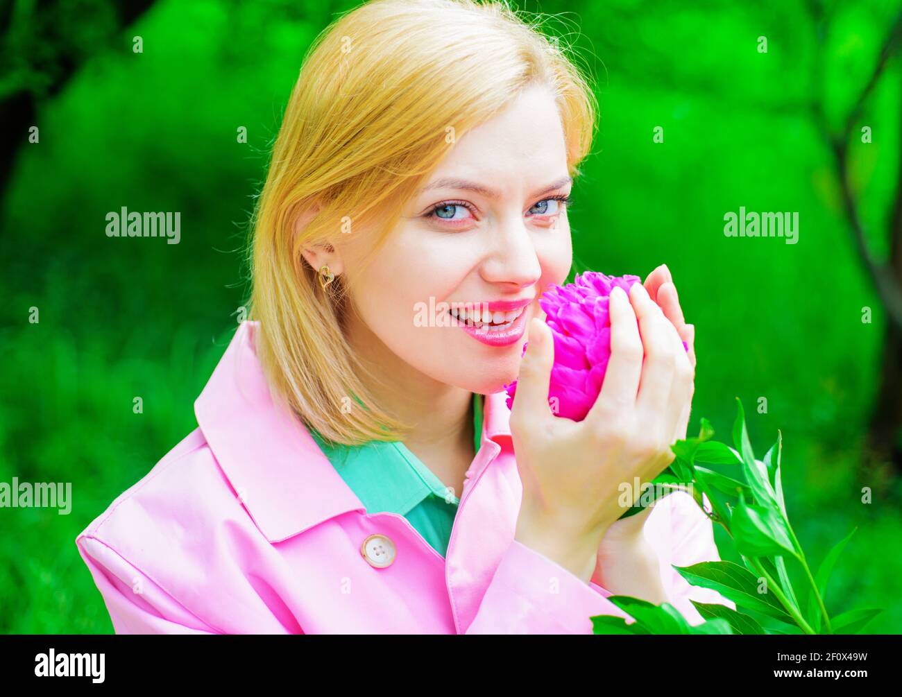 Nette Frau riecht Pfingstrose Blume. Schönes Mädchen mit rosa Blume. Romantische Frau im Frühling Park. Stockfoto