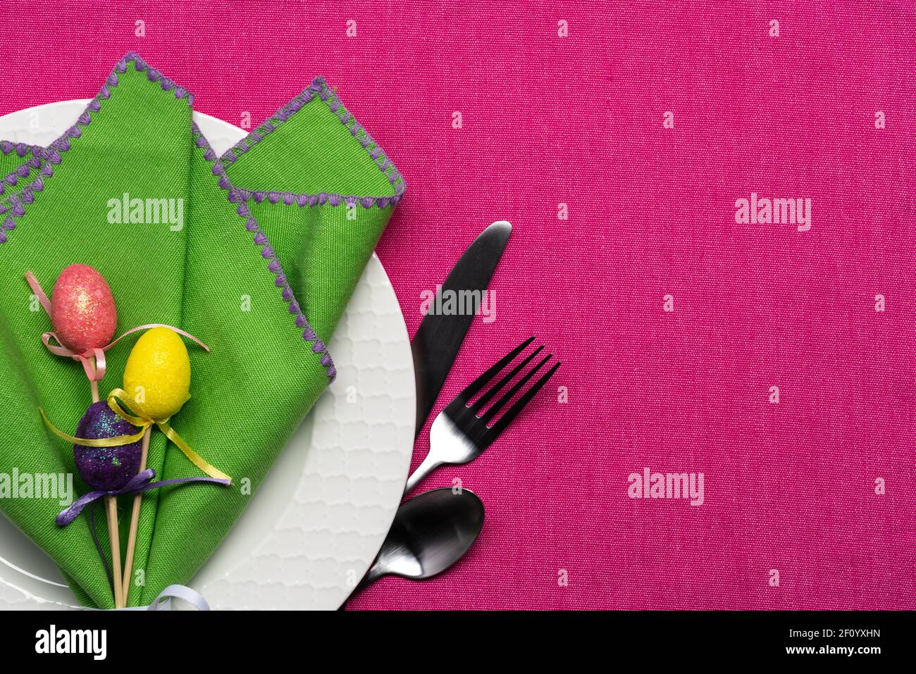 Helle Ostern oder Frühling Ort Einstellung eines weißen Korbflechten Musterteller mit grüner Serviette und Ei-Dekor auf einem Rosa Tischdecke Stockfoto