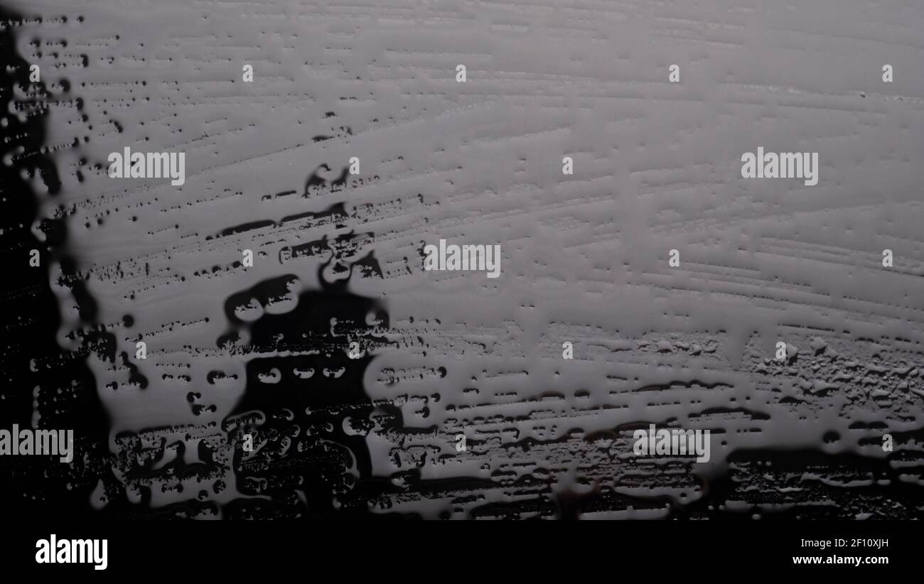 Wasser tropft auf Metalloberfläche. Wasser auf dem schwarzen Glas. Regen auf dem Glas in der Nacht. Stockfoto