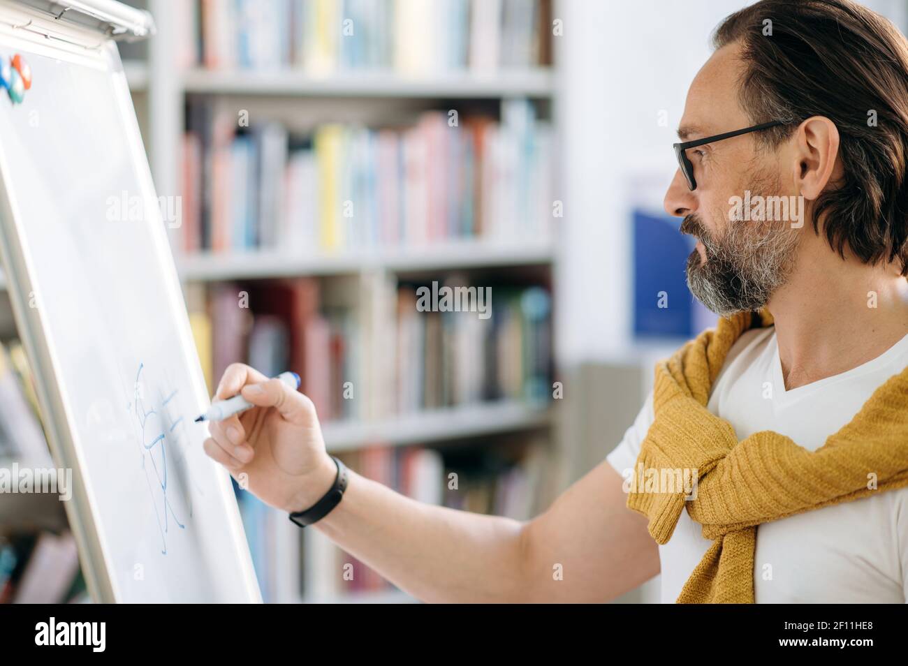 Konzentrierter kluger Kaukasier mittleren Alters, Lehrer oder Geschäftsleiter, schreibt Informationen auf einem Markiertafel während eines Vortrags Stockfoto