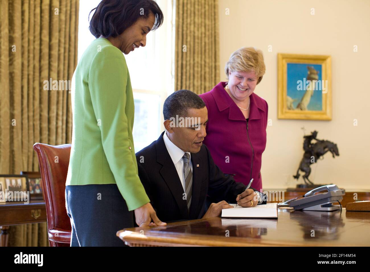 Die Vorsitzende des Wirtschaftsberaterrats, Christina Romer, und Cecelia Rouse, sehen zu, wie Präsident Barack Obama den Wirtschaftsbericht des Präsidenten im Oval Office unterzeichnet, 11. Februar 2010 Stockfoto