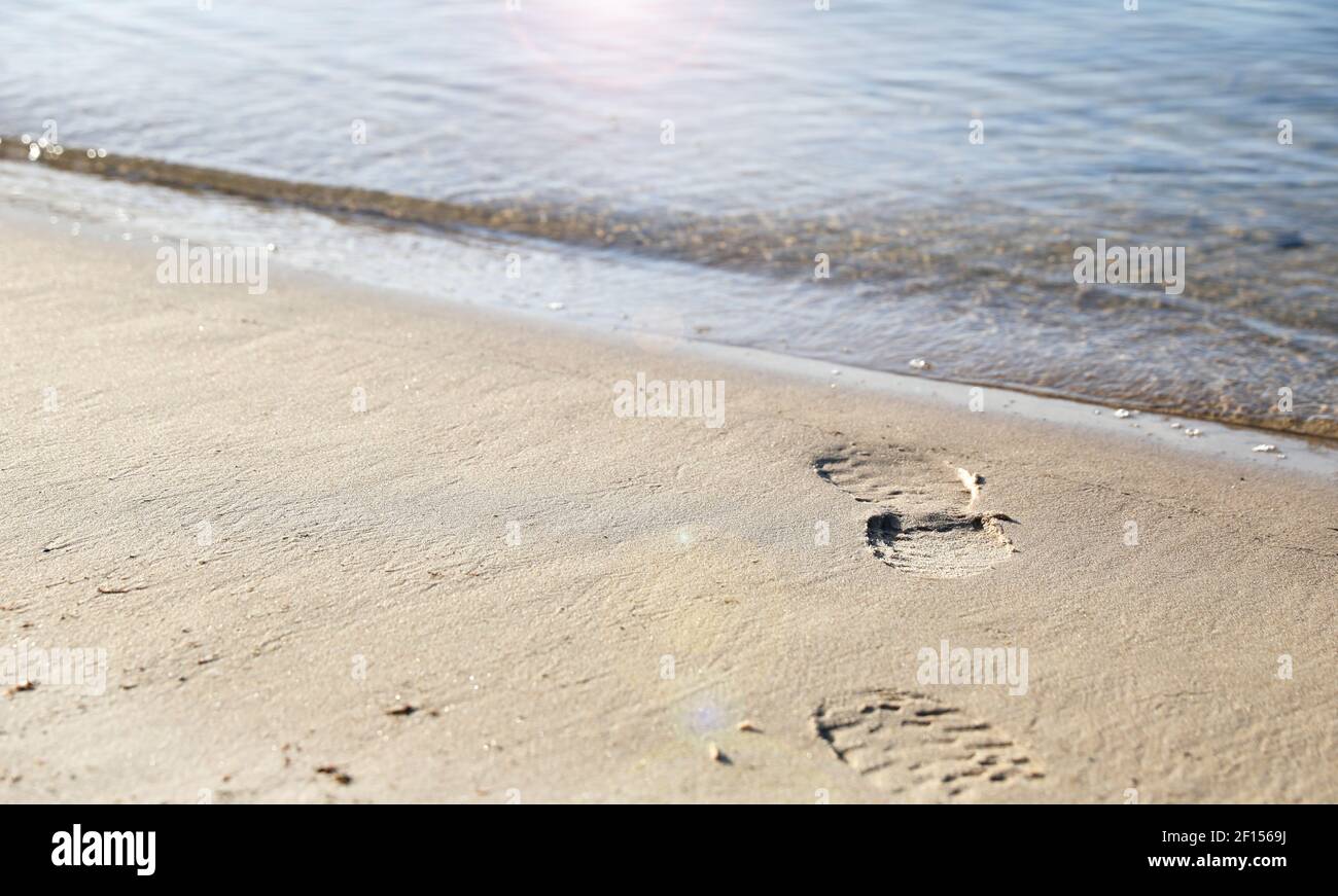 Subtiles Bild von Fußabdrücken, die Schuhe tragen, die zum Wasser gehen und nicht zurückkehren. Konzept von Tod, Selbstmord, Mordgeheimnis und Ertrinken. Stockfoto