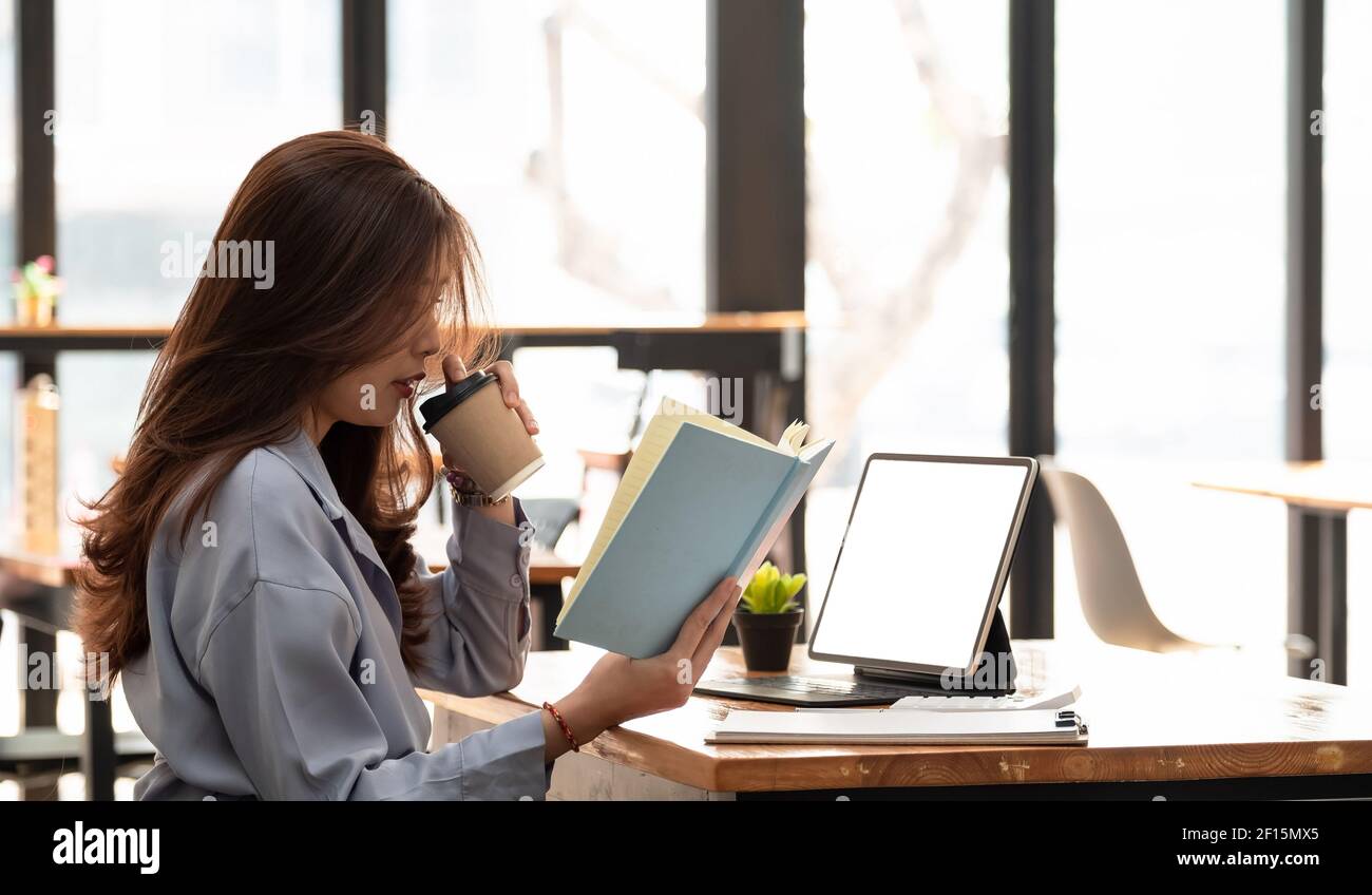 Asiatische Frau arbeitet mit Tablet beim Lesen von Daten auf Notebook. Student Mädchen zu Hause arbeiten. Arbeit oder Studium von zu Hause aus, freiberuflich, geschäftlich, Lifestyle Stockfoto