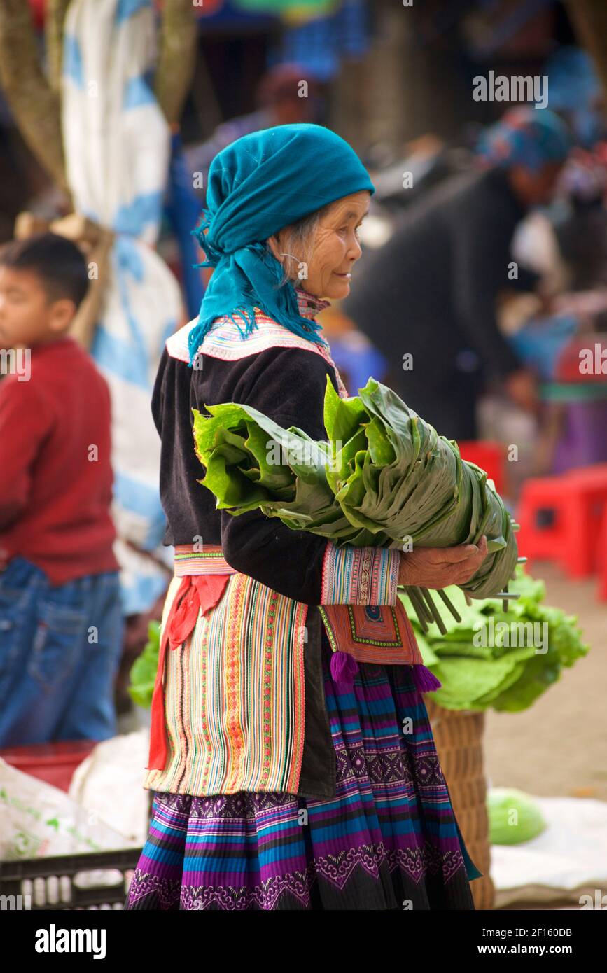 Ältere Blume Hmong Frau in Stammeskleidung auf dem Markt mit einem Gelege von Palmblättern. BAC Ha, Lao Cai Provinz. nordvietnam Stockfoto