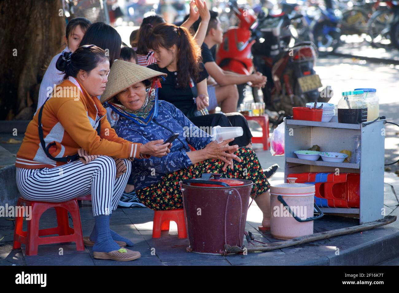 Vietnamesisches Straßenleben. Anbieter verkaufen Snacks am Wasser, Hoi an, Vietnam. Teilen eines Smartphones Stockfoto