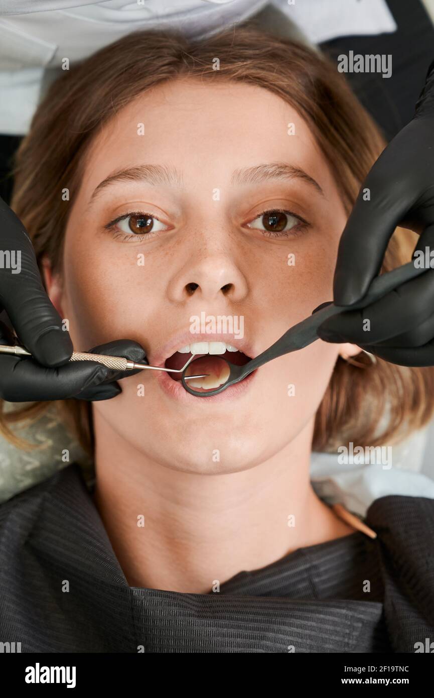 Nahaufnahme der Zahnarzthände Überprüfung weiblichen Patienten Zähne mit Zahnspiegel und Explorer. Junge Frau mit prophylaktischen Untersuchung in der Zahnklinik. Konzept der Zahnmedizin, Zahnpflege. Vertikale Aufnahme. Stockfoto