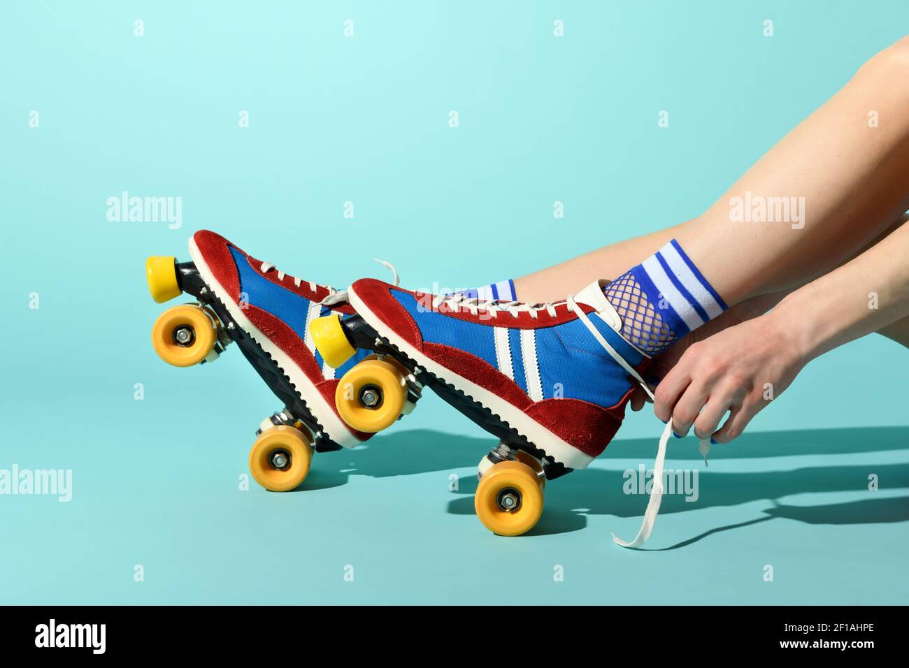 Junge Frau, die die Schnürsenkel in Rot und Blau festbindet Rollerskates mit bunten gelben Rädern in einer Nahaufnahme Blick auf ihre Füße und Hände über einen blauen Bac Stockfoto
