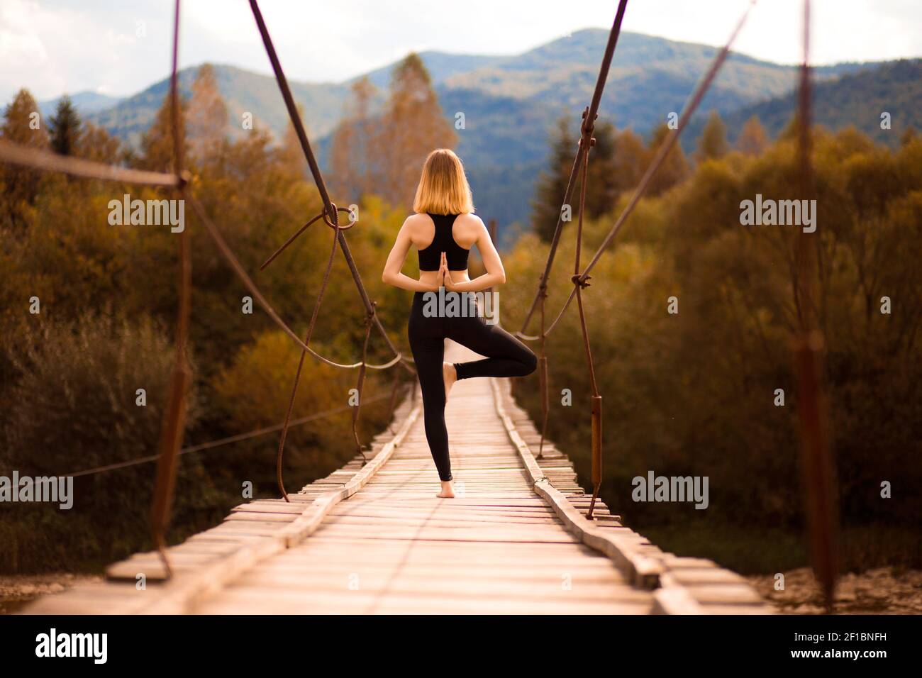 Yoga im Freien. Ruhige Frau, die Yoga-Balance-Übungen macht. Yoga-Meditation auf Brücke über den Fluss mit Bergen Hintergrund. Konzept der gesunden Lebensweise und Entspannung. Stockfoto