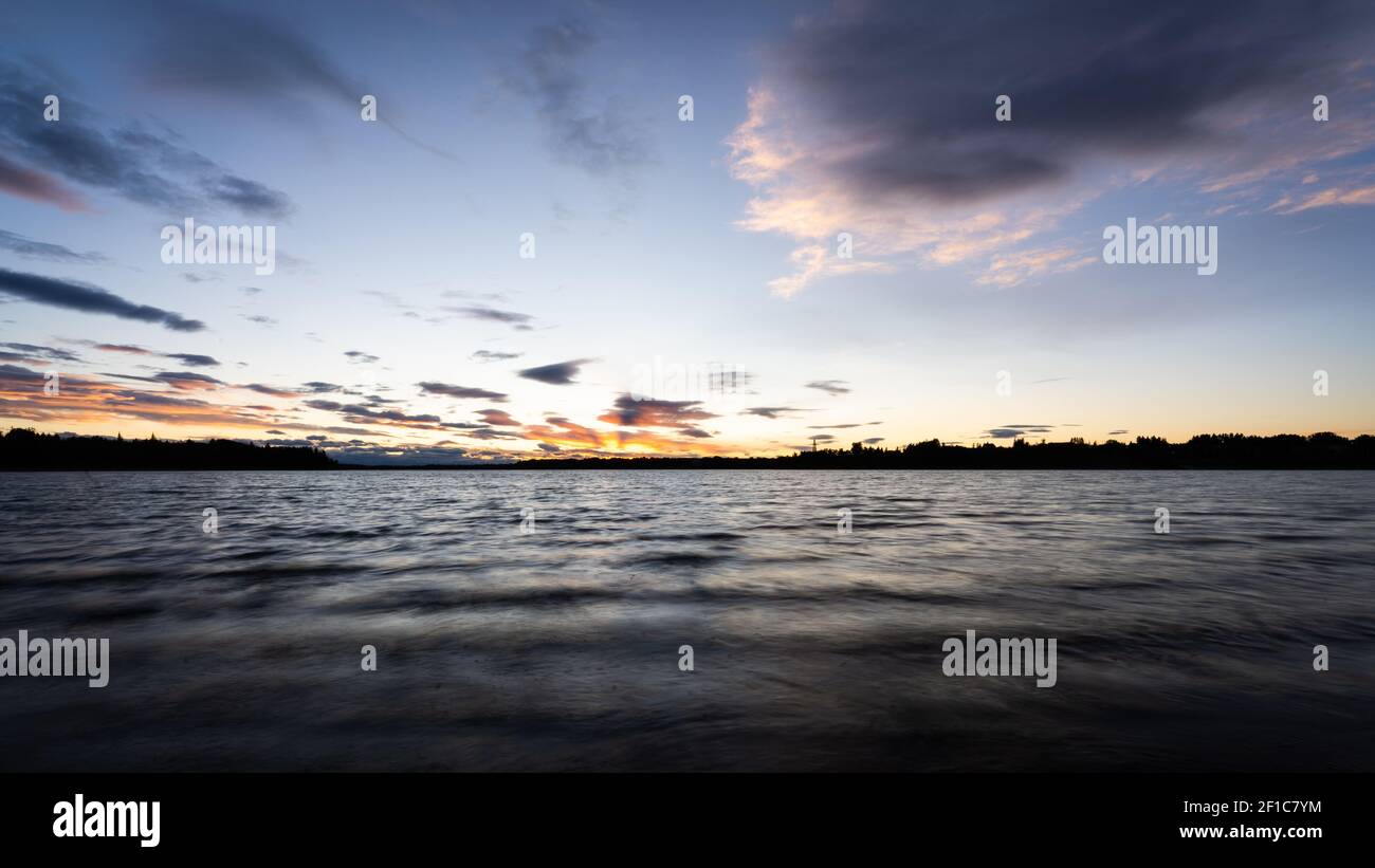 Farbenfrohe Sonnenuntergänge über dem See, aufgenommen als Langzeitbelichtung in Calgary, Alberta, Kanada Stockfoto