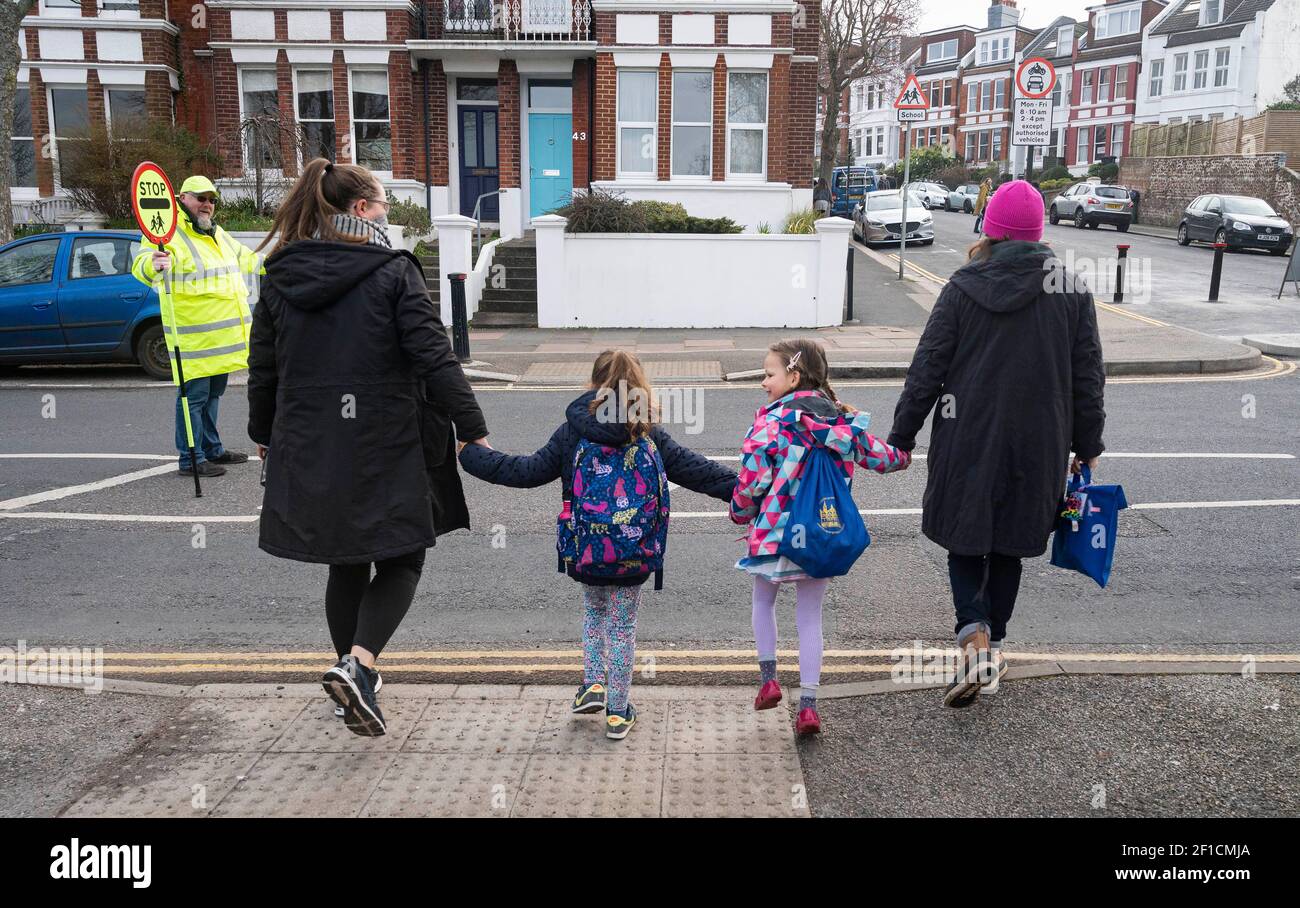 Brighton UK 8th March 2021 - der Lollipop-Mann Simon Moss begrüßt heute Morgen Kinder in der St. Luke's Primary School in Brighton, da die Sperrbeschränkungen der Regierung in England allmählich gelockert werden. Schulen und Colleges werden für alle Schüler heute in ganz England wieder geöffnet : Credit Simon Dack / Alamy Live News Stockfoto