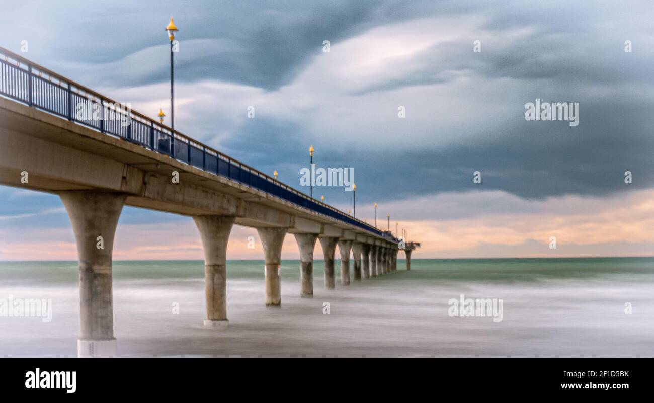 Massiver Betonsteg, der von links zum Horizont führt, umgeben vom Ozean, Langzeitaufnahme in New Brighton Beach in Christchurch, Neuseeland Stockfoto