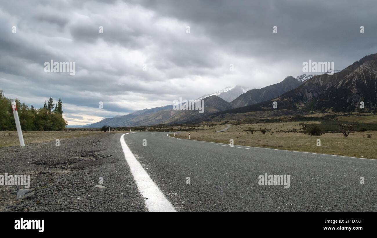 Straße, die in Richtung Berge führt, mit bewölktem Himmel. Low Perspective Aufnahme aus dem Aoraki Mt Cook National Park in Neuseeland Stockfoto