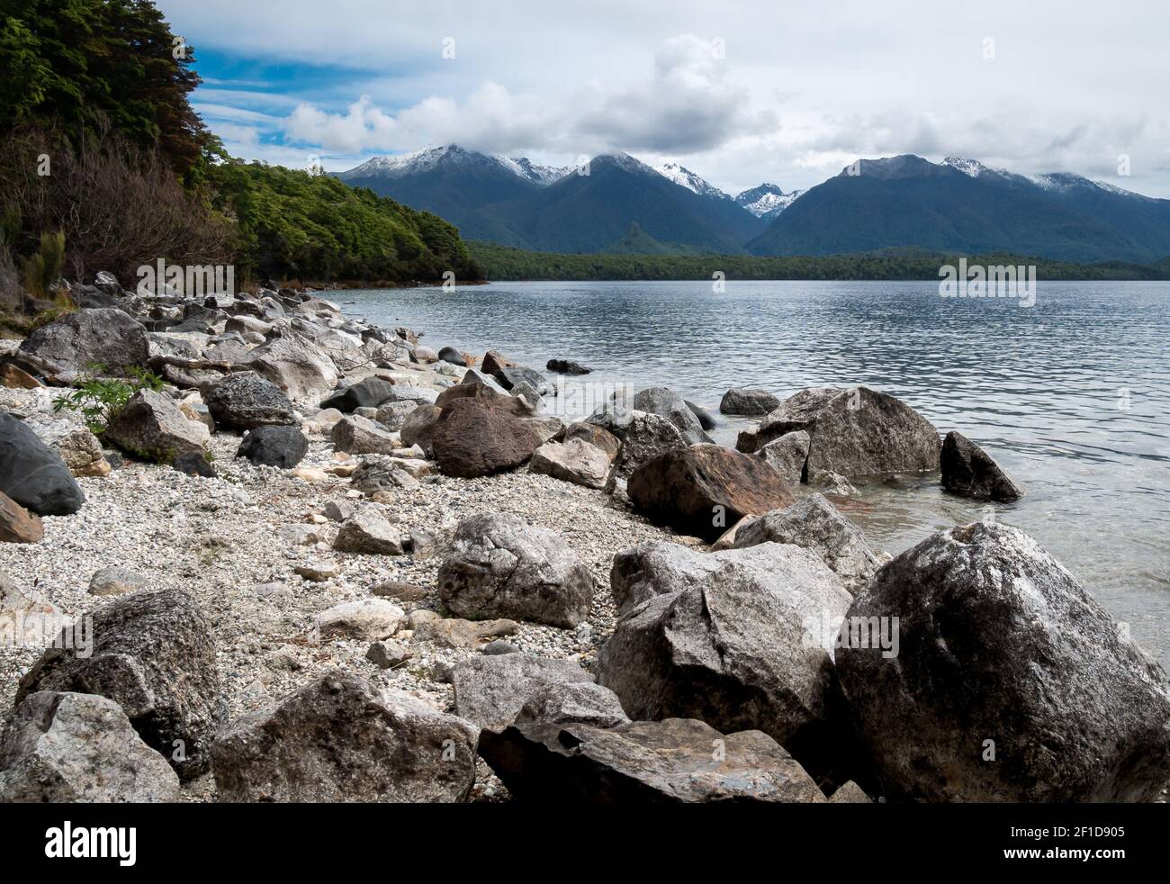 Felsige Seeufer mit Bergen im Hintergrund, aufgenommen am Lake Manapouri, Fiordland National Park, Neuseeland Stockfoto