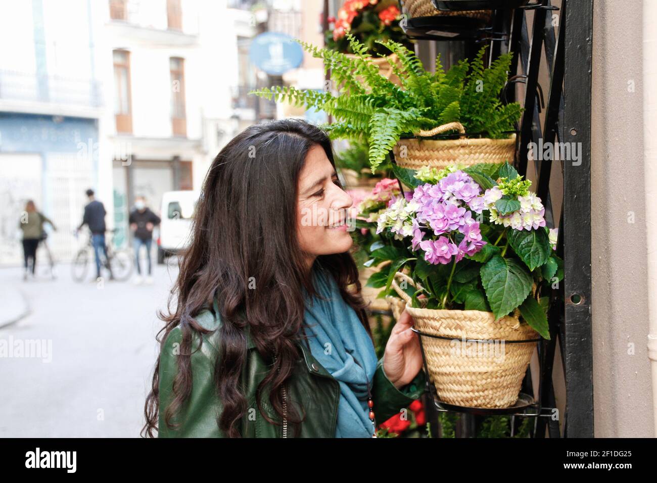 Spanisch attraktiv hübsch mittleren Alters Brünette Frau riecht Blumen aus Ein Blumenhändler auf der Straße Stockfoto