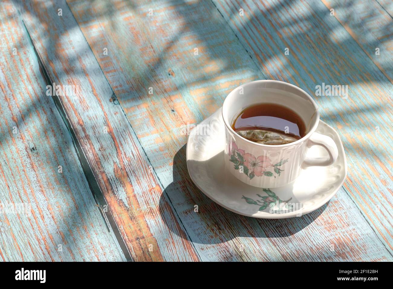 Tasse Tee auf rustikalem Holztisch mit Schatten von Palmblättern. Stockfoto