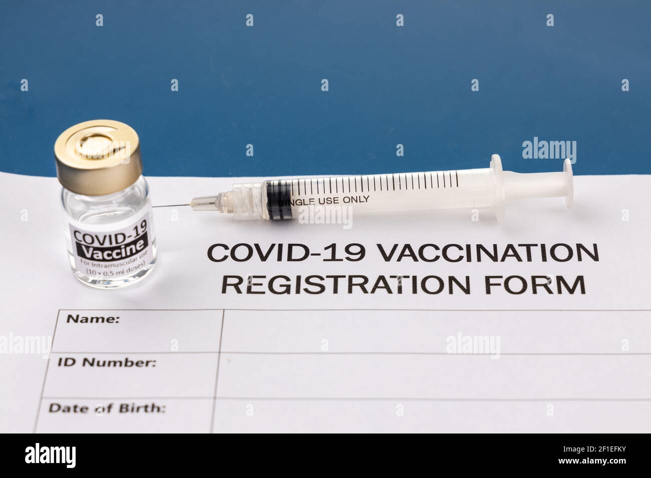 Covid-19 Impfformular mit Fläschchen und Spritze auf blau Schreibtisch Stockfoto