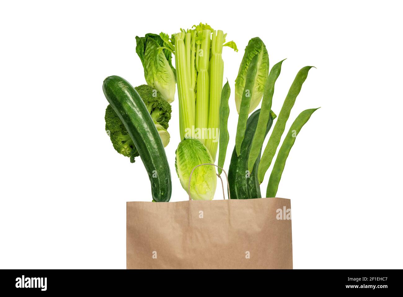 Grün gefärbtes Gemüse fliegend aus der Kraftpapier-Einkaufstasche Isoliert auf Weiß Stockfoto