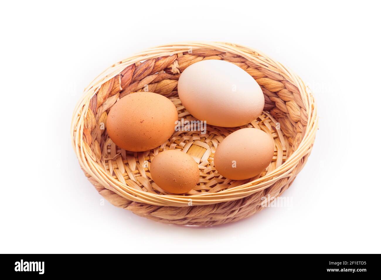 Eier - vier Hühnereier unterschiedlicher Größe in einem kleinen Korbkorb, isoliert auf weißem Hintergrund Stockfoto