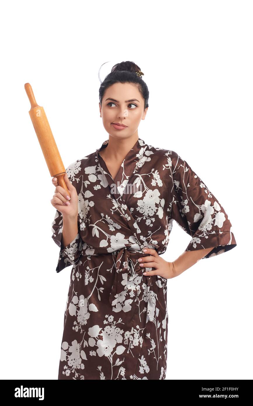 Schöne Hausfrau in Hausgewand mit Haar bun hält Holz Rollholz über weißem Hintergrund. Konzept der täglichen Routine und Aufgaben. Stockfoto