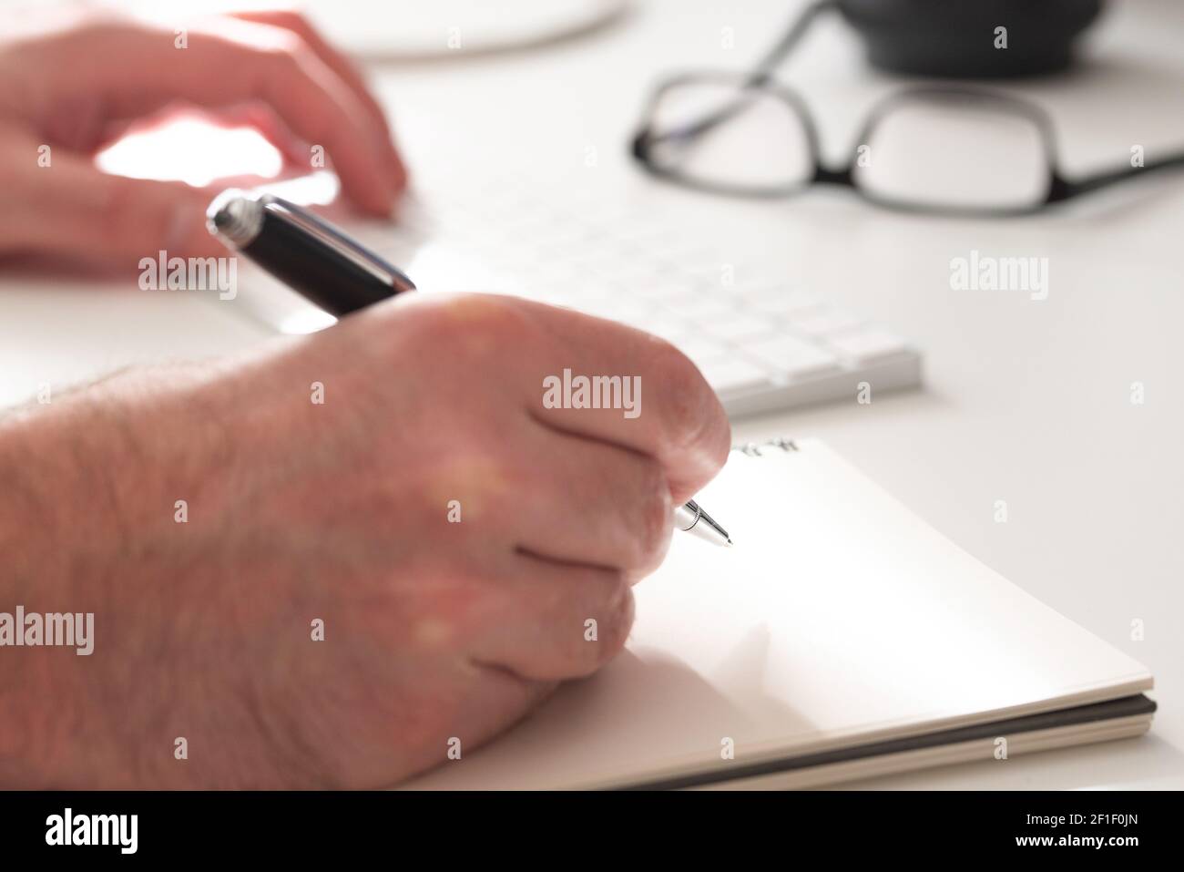 Nahaufnahme der Hände einer Person, die auf Papier notiert wird, weißes Tippen auf Computertastatur, Geschäftskonzept Stockfoto