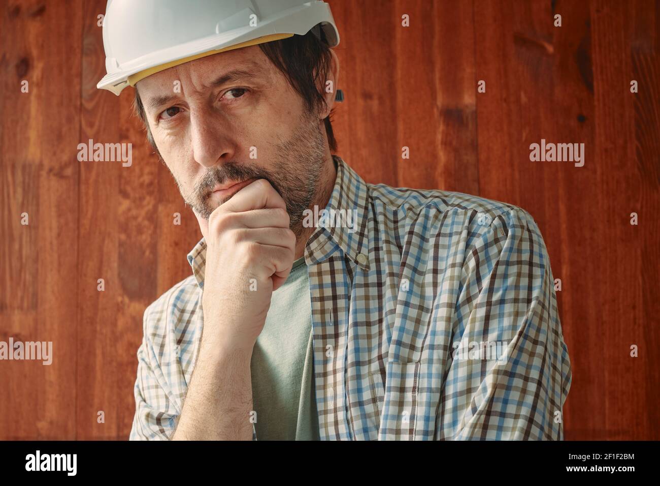 Porträt von nachdenklichen männlichen Arbeiter mit weißem Schutzhelm, Beschäftigung und Arbeitskonzept, Blick auf die Kamera Stockfoto
