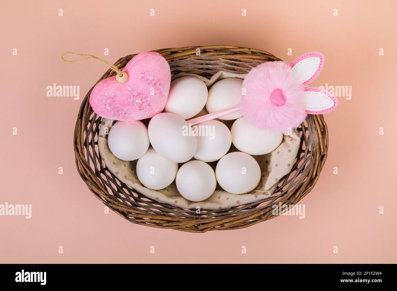 Ostern. Weiße Eier in einem Korb mit einem künstlichen Kaninchen, auf einem einheitlichen rosa Hintergrund. Für Text platzieren. Stockfoto