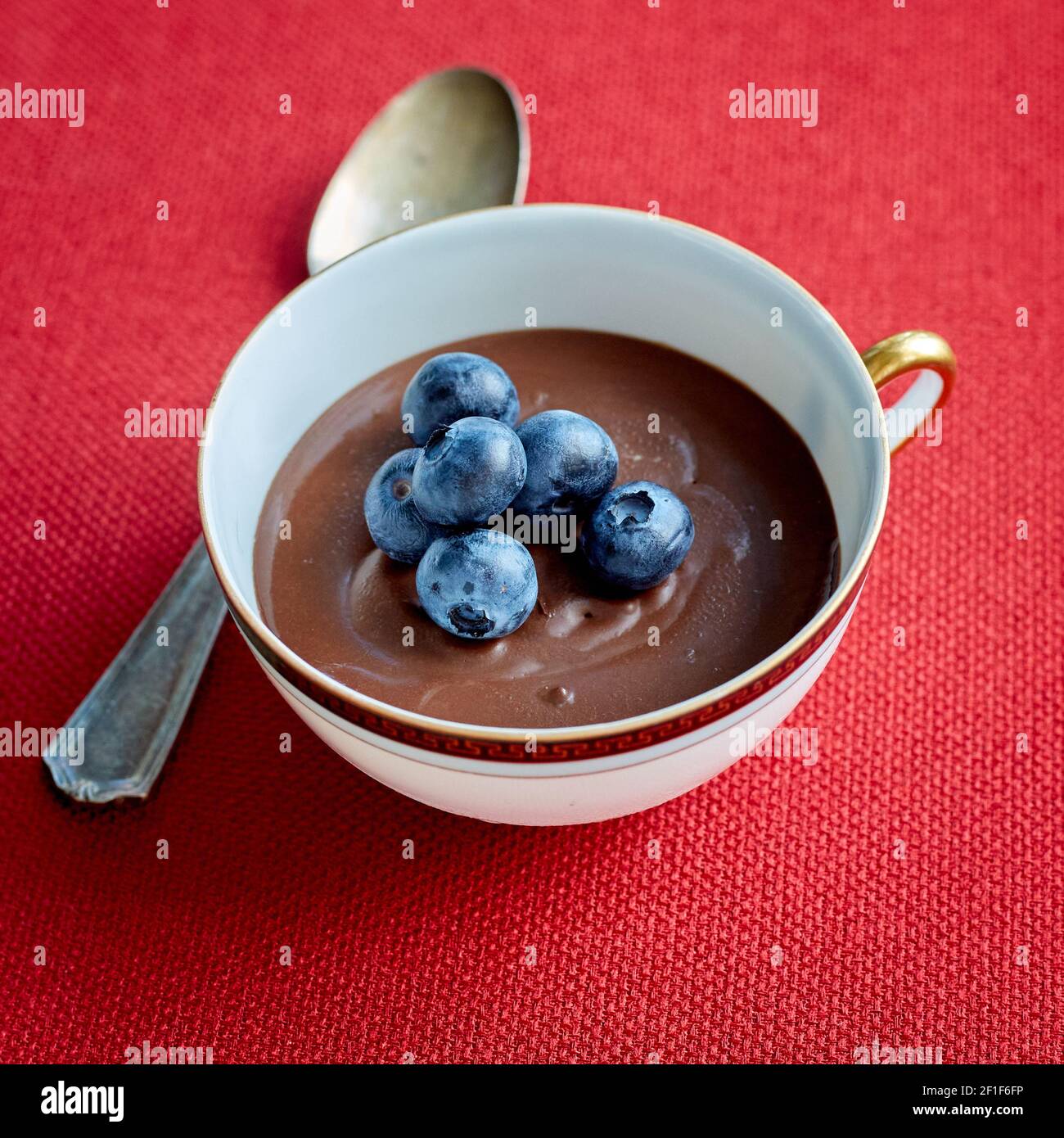 Schokoladenmousse mit frischen Heidelbeeren in einer Tasse mit Metall Löffel auf rotem Stoffset Stockfoto