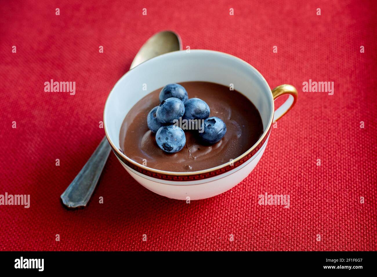 Schokoladenmousse mit frischen Heidelbeeren in einer Tasse mit Metall Löffel auf rotem Stoffset Stockfoto