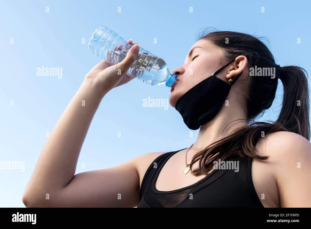 Junge kaukasische Frau, die sich selbst mit Wasser aus einer Flasche unter dem klaren Himmel in Kuba versorgt Stockfoto