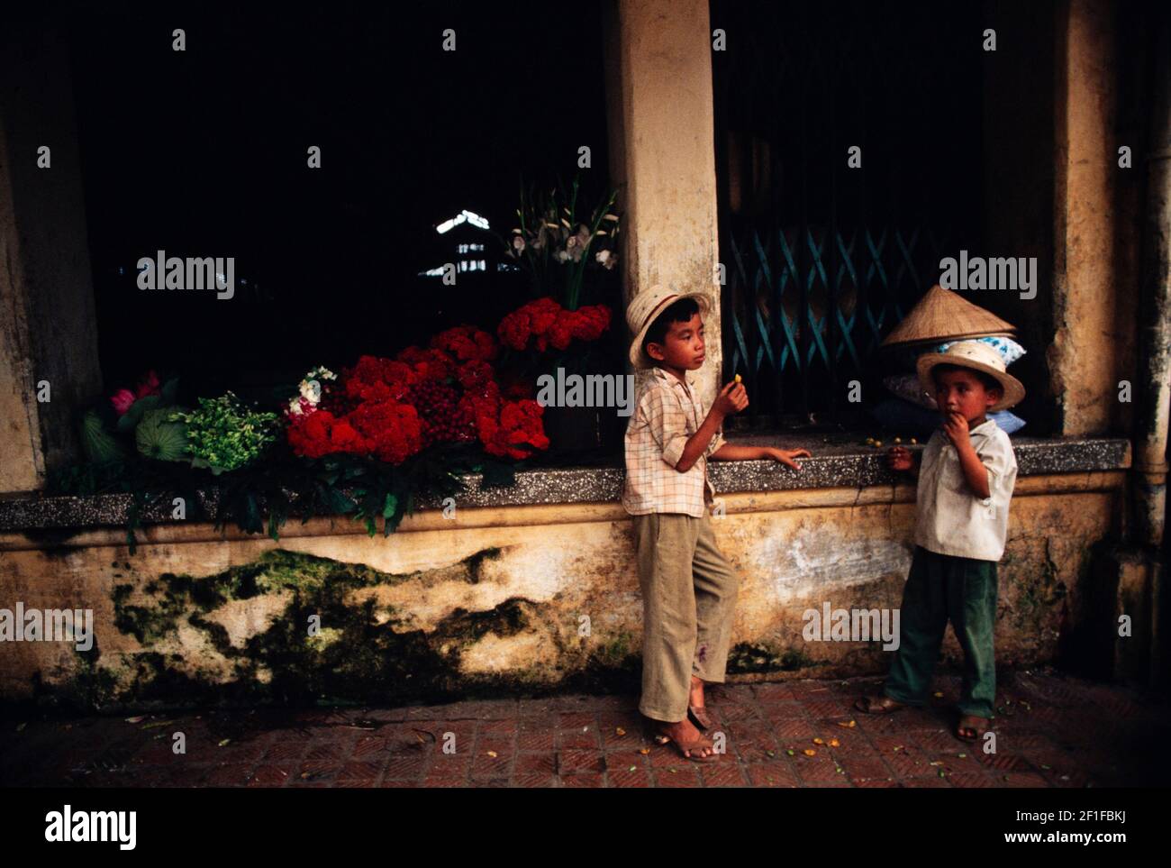Jungen essen einen Snack, während sie sich an den Blumenstand ihrer Mutter erinnern, Hanoi, Nordvietnam, Juni 1980 Stockfoto