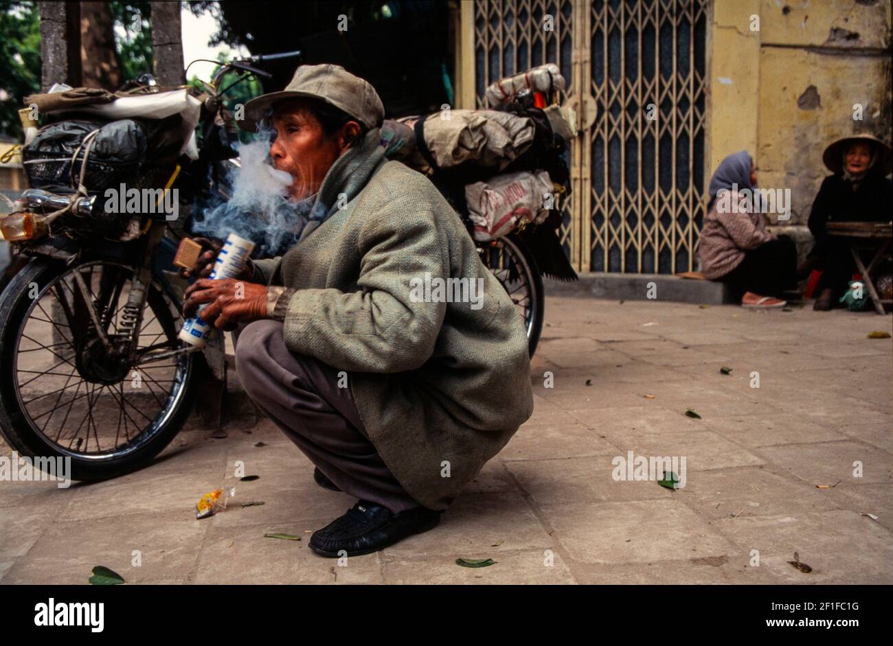 Ein umherziehender Motorradfahrer, der Opium an einer Straßenecke raucht, Hanoi, Vietnam, Juni 1980 Stockfoto