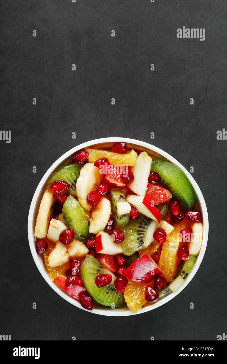 Frischer Obstsalatbecher aus saftigen Früchten auf schwarzem Hintergrund. Freier Speicherplatz für Text. Scheiben von frischen, saftigen und gesunden Früchten für eine gesunde Ernährung. Stockfoto