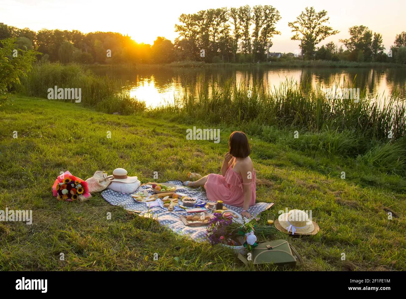 Eine junge Frau sitzt auf einem Picknick in einem Park Am Ufer eines Flusses Stockfoto