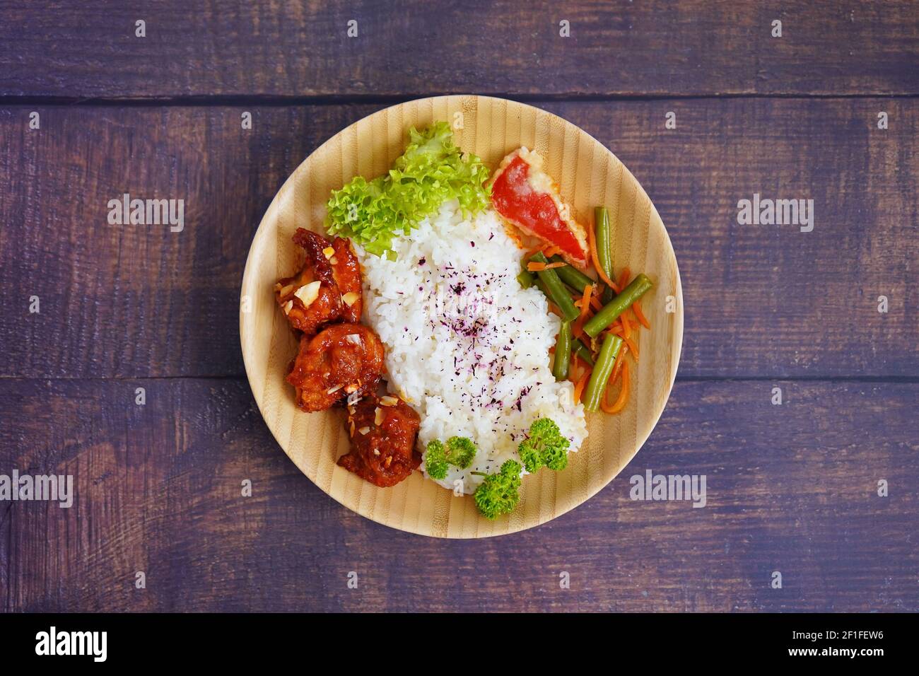 Hausgemachtes japanisches gegrilltes Hähnchengericht mit Gemüse und Reis, serviert auf einer Bambusplatte. Rustikale Holztisch Hintergrund. Stockfoto