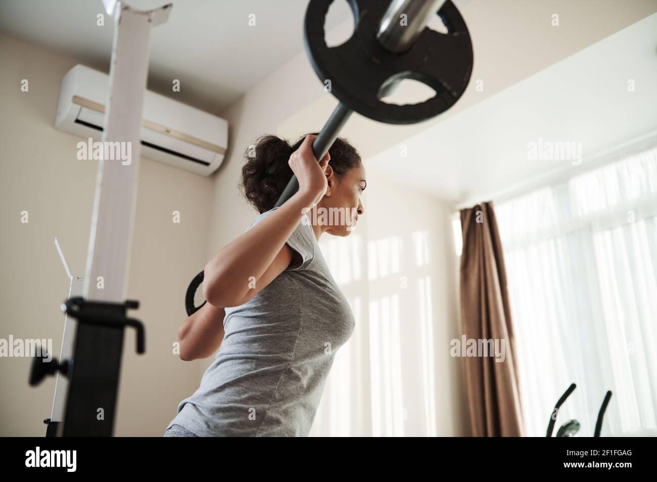 Rückansicht zu afrikanischer junger sportlicher Frau, die schwere Hocke in Heimturnierhalle mit Langhantel tut. Bodybuilding. Stockfoto