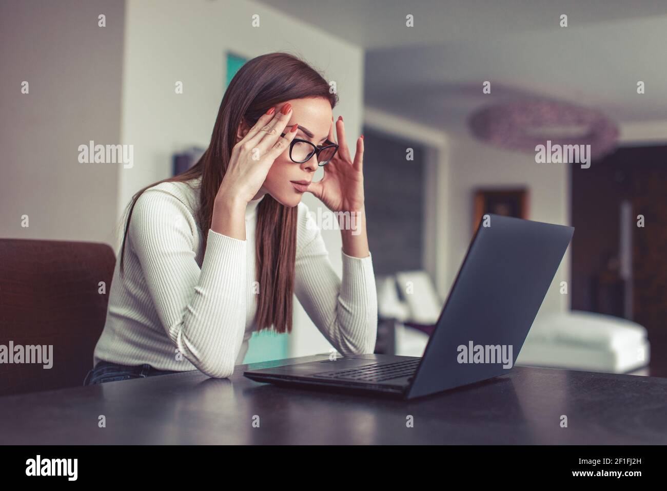 Intelligente junge kaukasische Frau, die sich auf die Arbeit am Laptop im Heimbüro, drinnen konzentriert Stockfoto