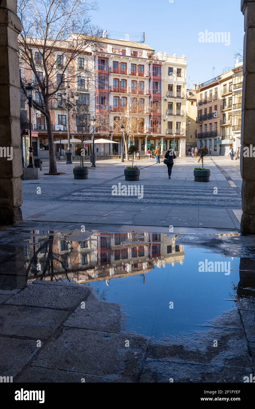 Toledo, Spanien - 28. Februar 2021: Geschäftiges Zocodover-Quadrat in Toledo mit Reflexionen in einer Wasserpfütze im Vordergrund Stockfoto