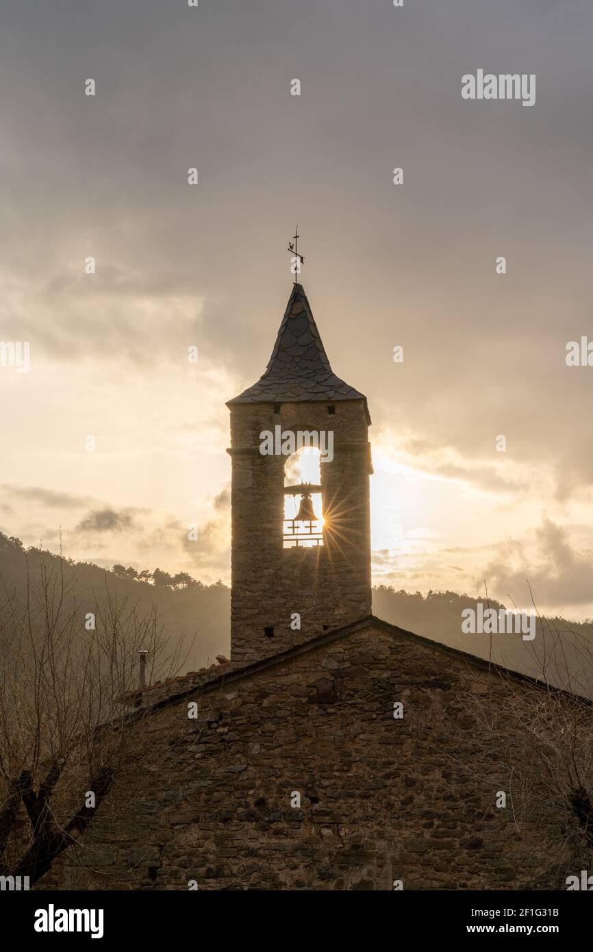 Eine massive Bergkirche aus Stein mit Kirchturm und Sonne Stern, der im Winter unter einem bewölkten Himmel durchscheint Abend Stockfoto
