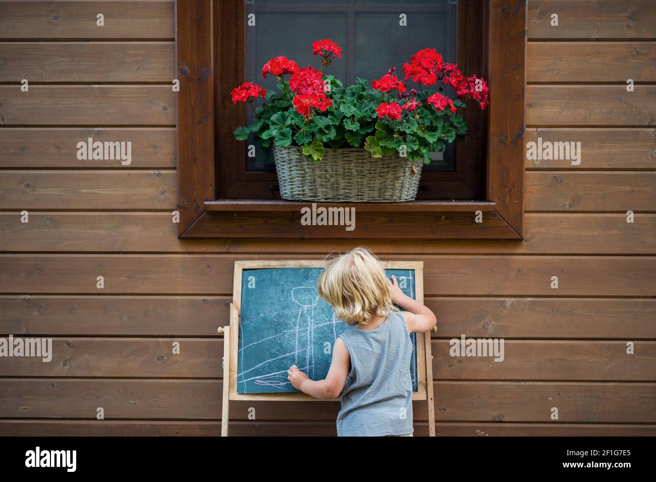 Rückansicht des glücklichen kleinen blonden Jungen, der im Sommer im Freien von Haus spielt. Stockfoto
