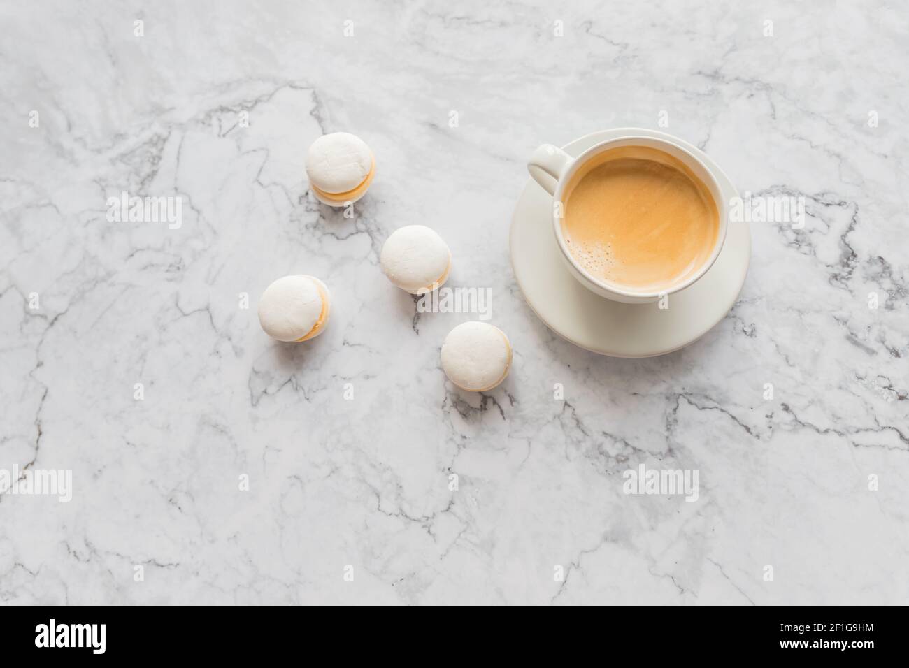 Kaffee und Französisch Makronen auf Marmor Hintergrund.Tasse aromatischen Kaffee Cappuccino mit weißen Plätzchen und bestreuten Körnern von natürlichen gerösteten Kaffee Stockfoto
