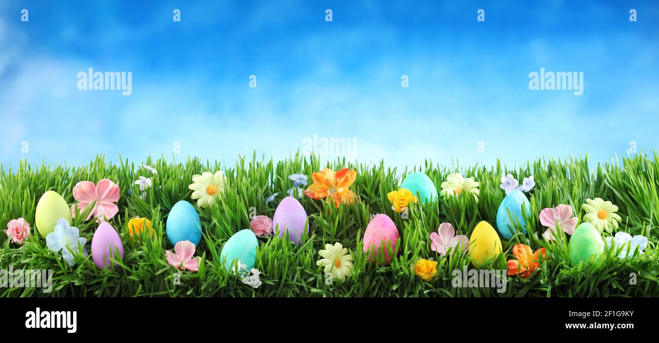 Leuchtend bunte Ostereier auf grünem Gras mit Blumen gegen den blauen Himmel Stockfoto
