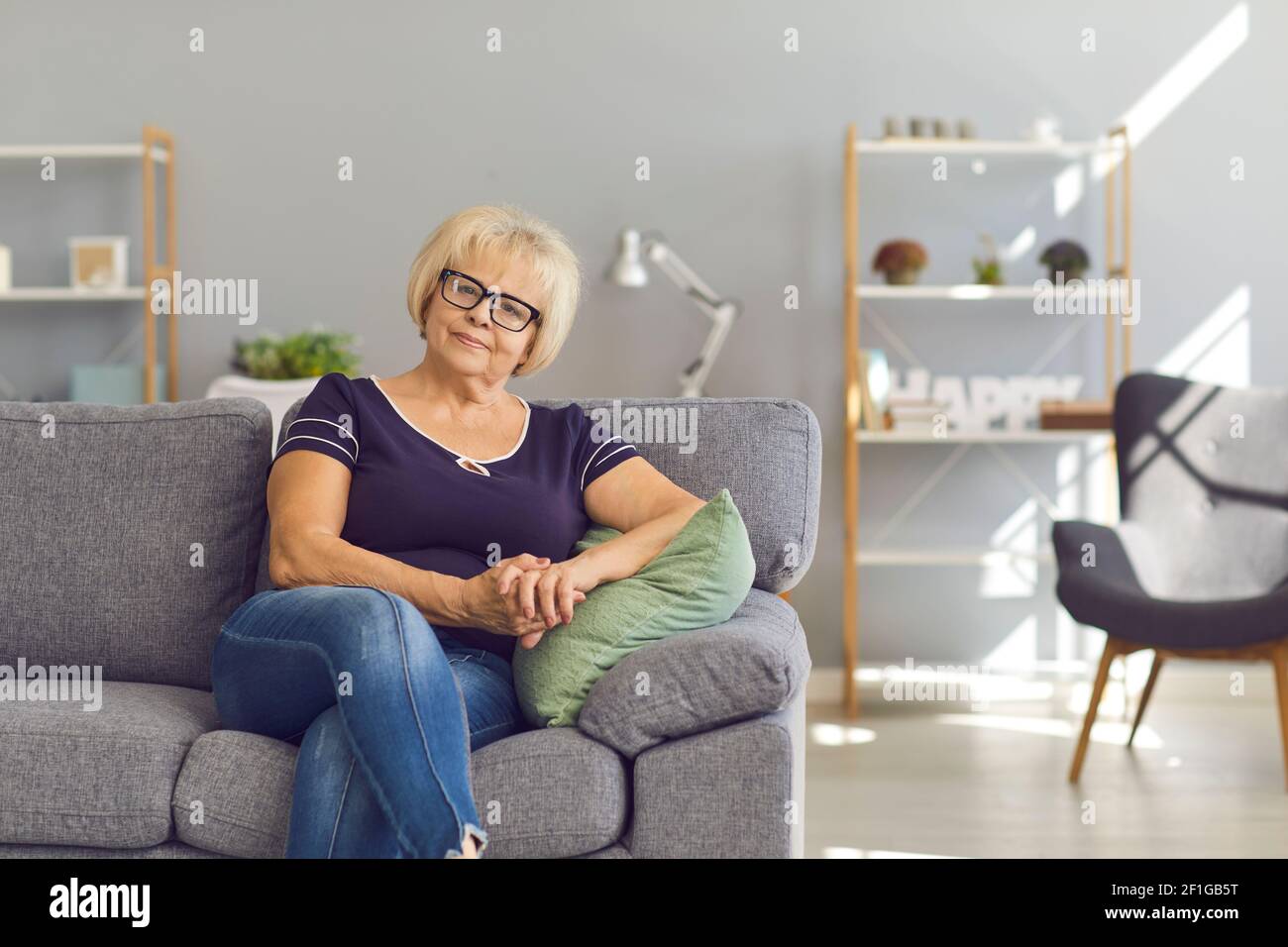Lächelnde reife Frau oder Großmutter, die zu Hause auf dem Sofa sitzt Stockfoto
