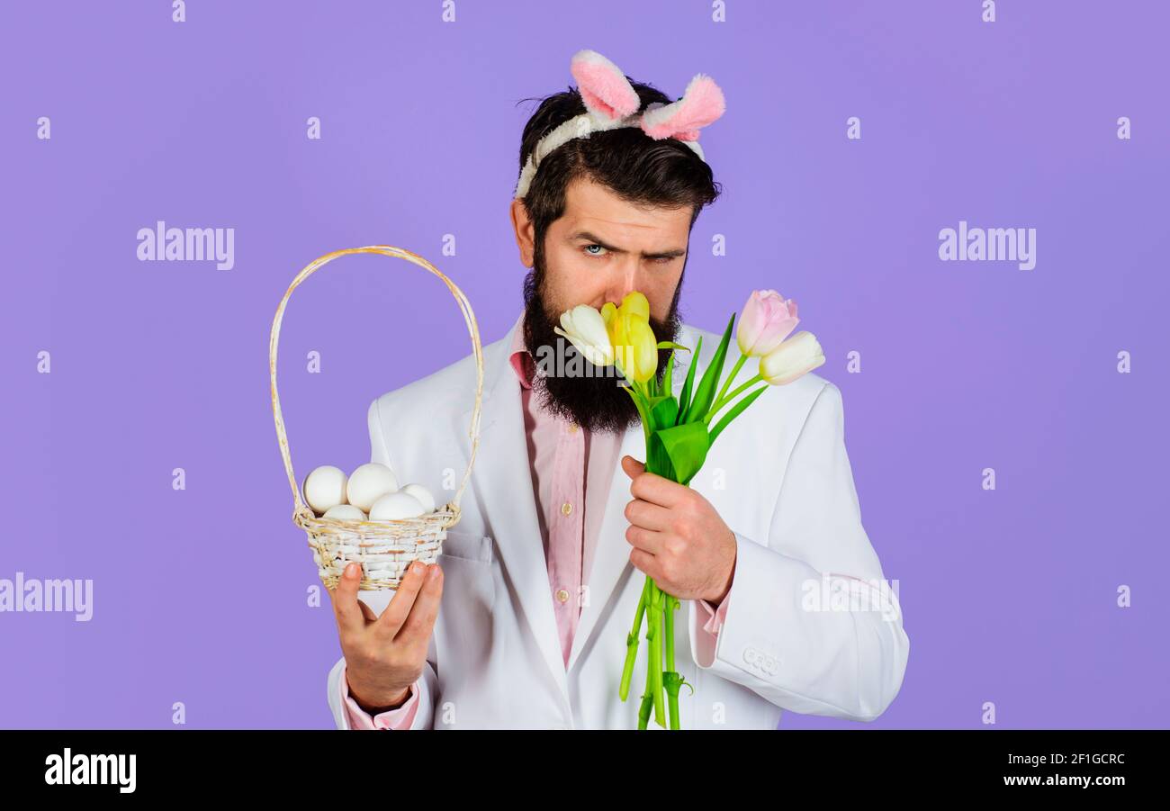 Ostertag. Mann mit Tulpenstrauß mit Korbeiern. Schöner bärtiger Rüde mit Hasenohren. Stockfoto