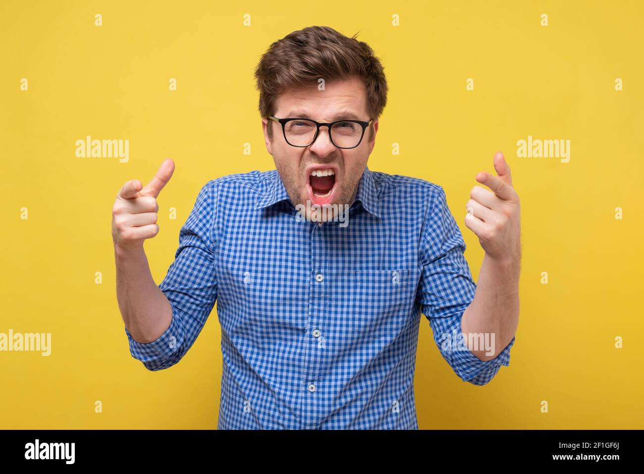 Kaukasischer Mann in Brille schreiend und schreiend. Studio auf gelber Wand. Negative menschliche Emotionen im Gesicht Stockfoto
